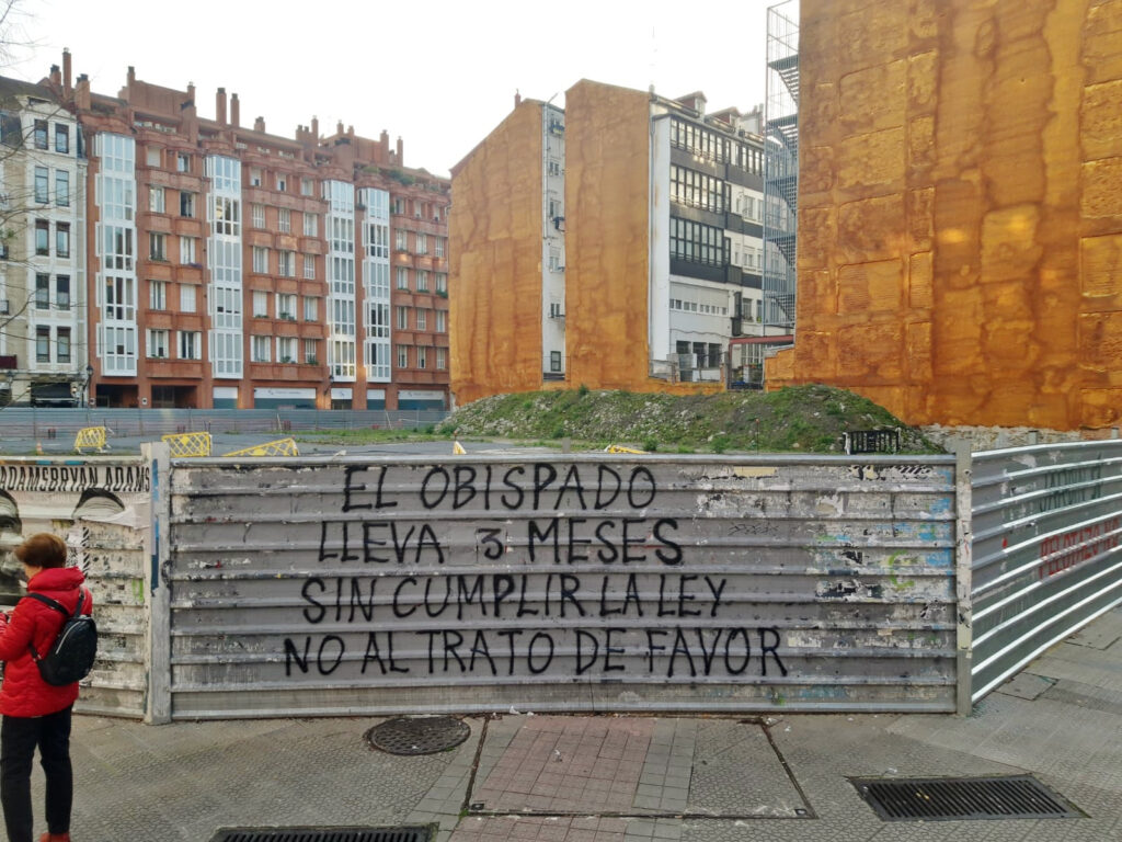 Valla de obra en la que aparece una pintada en la que se indica que el Obispado de Bilbao lleva 3 meses sin cumplir con las resoluciones municipales y que esto upone un trato de favor.