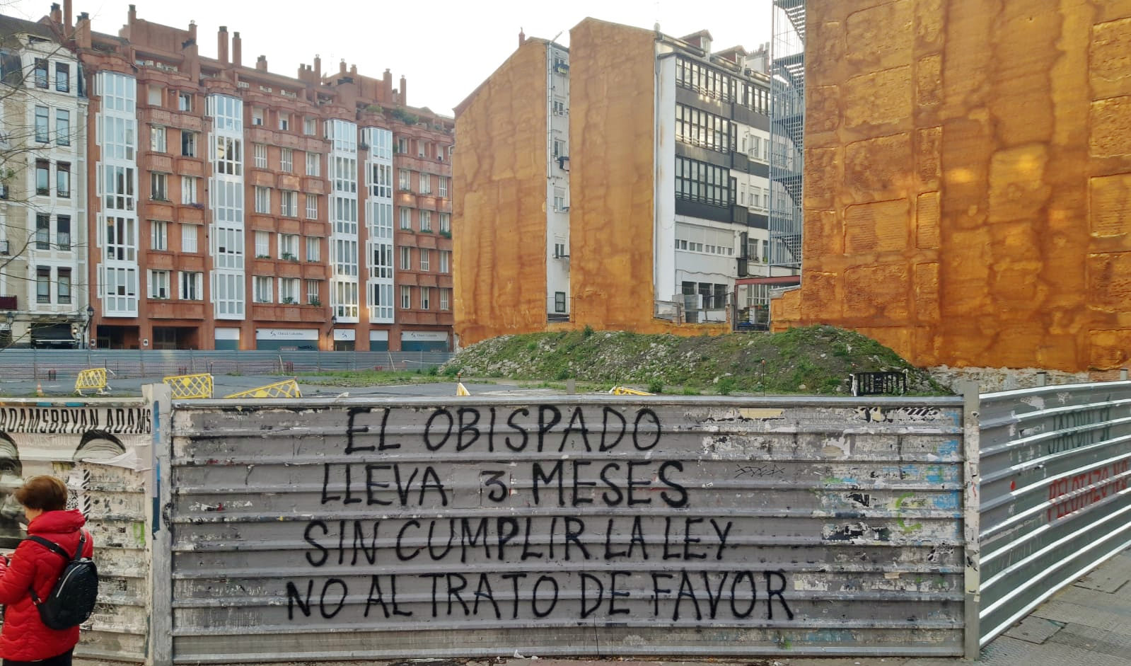 Valla de obra en la que aparece una pintada en la que se indica que el Obispado de Bilbao lleva 3 meses sin cumplir con las resoluciones municipales y que esto upone un trato de favor.